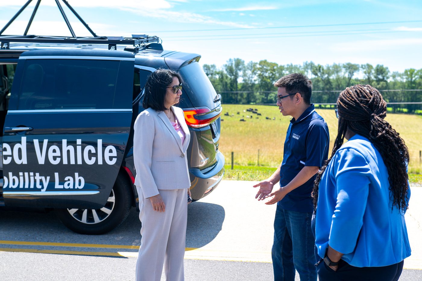 Lab members and President Bendapudi talking beside the automated vehicle on the test track