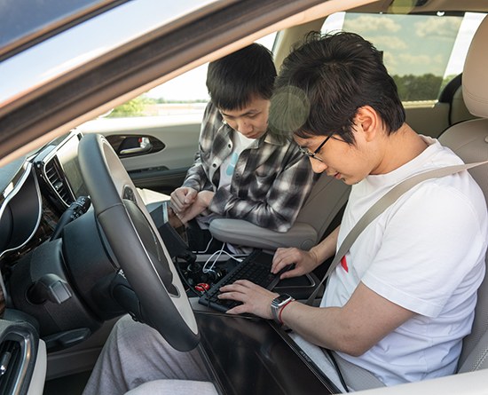 Yuxin Ding and Chenxi Chen working on a laptop in the driver’s seat of the lab’s automated vehicle